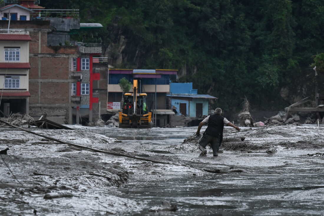 A resident walks along a street covered in mud following flash floods and a landslide disaster in Devighat, in Nepal's Nuwakot district on August 26, 2026. A massive flood and landslide disaster on the Nepal-Tibet border killed at least 103 people on August 26, 2026 and left several hundred missing, many of them foreign tourists. Aid workers said entire settlements had been "wiped out". Some 403 tourists -- 341 of them foreigners -- were unaccounted for several hours after the disaster struck, according to the tourism ministry. (Photo by PRAKASH MATHEMA / AFP via Getty Images)